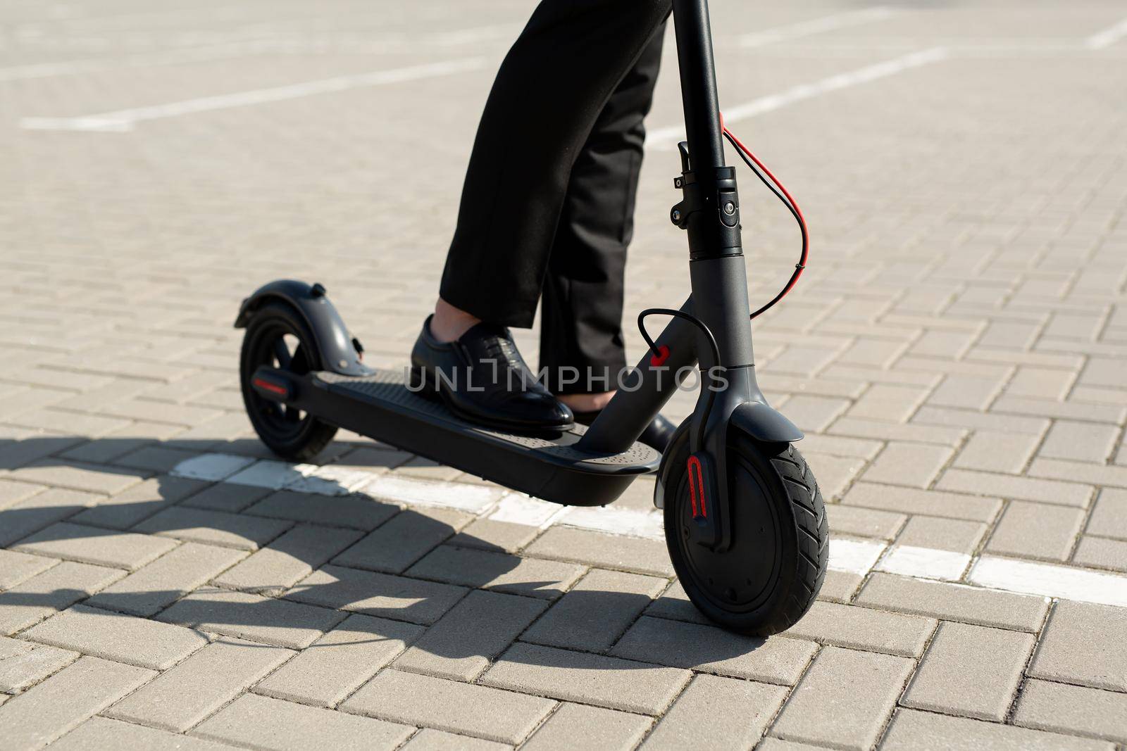 Close-up of a man's feet in a business suit and shoes near an electric scooter by StudioPeace