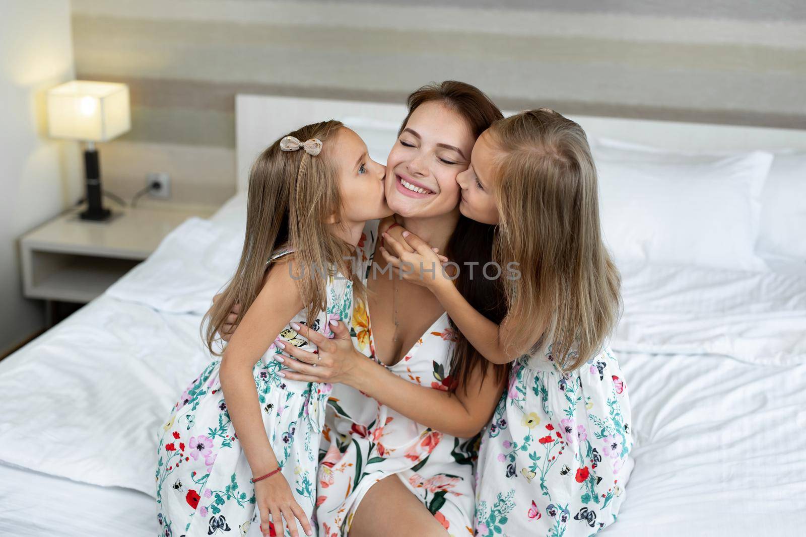 Twin girls kiss their mom in a hotel room