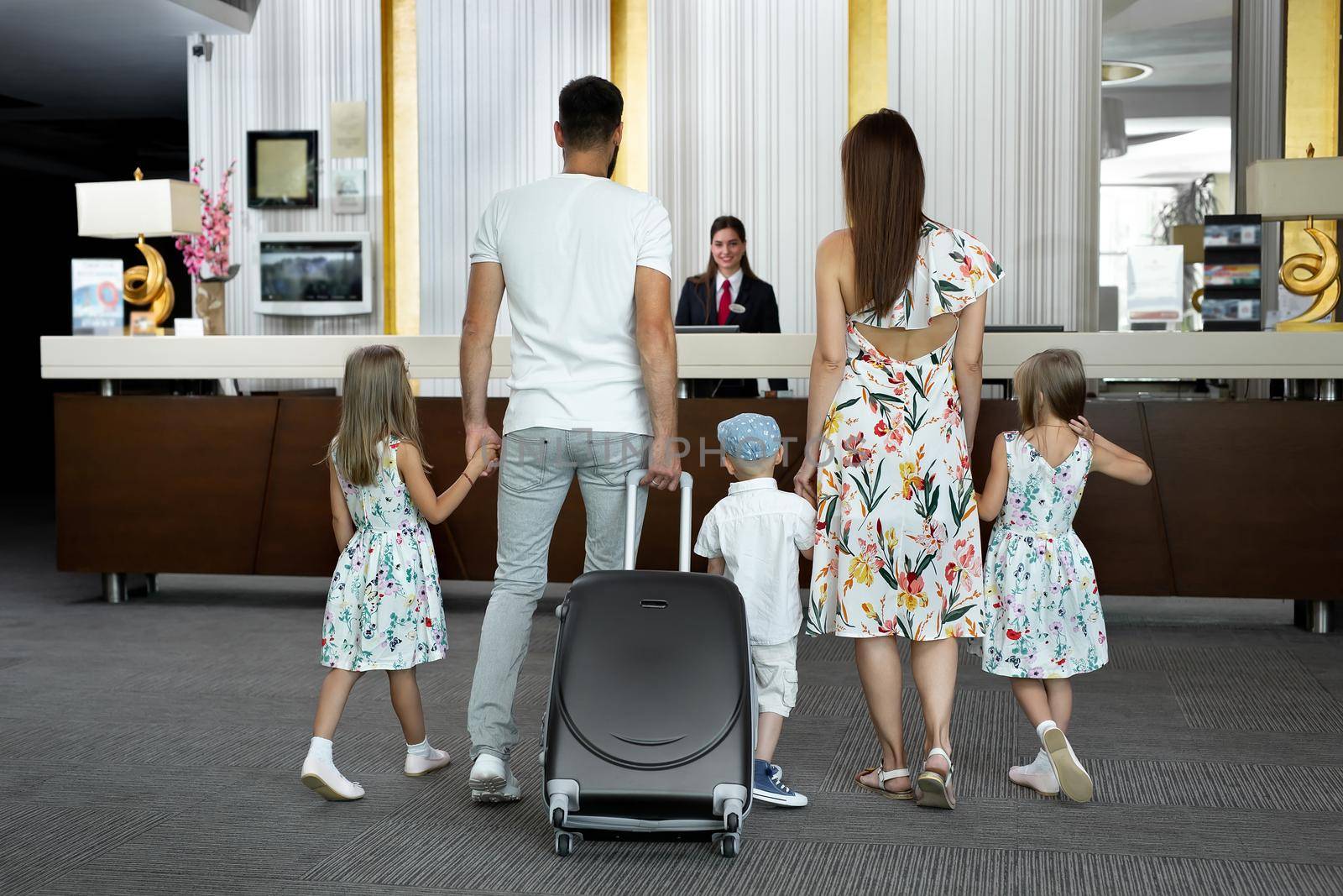 Family of five enters to the hotel lobby to check in at the reception for vacation.