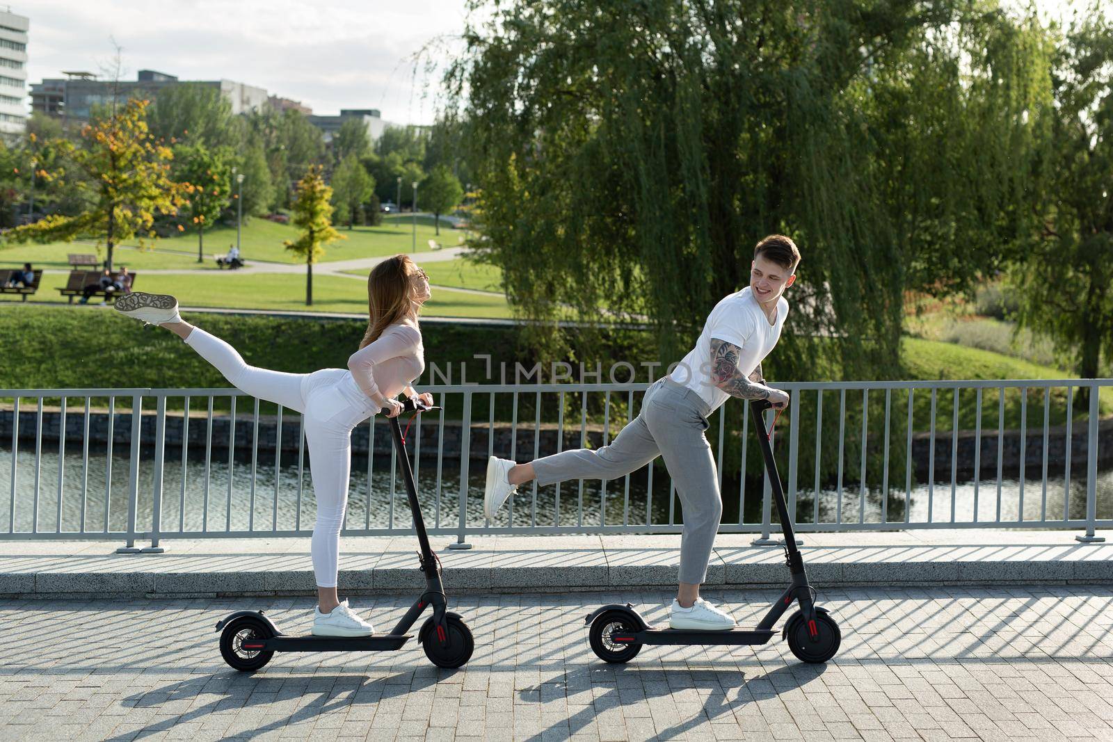 Young couple on vacation having fun driving electric scooter through the park. by StudioPeace