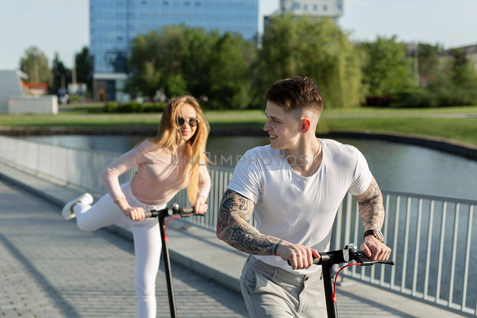 Beautiful young couple is enjoying sunny summer day while riding their own electro scooters by StudioPeace