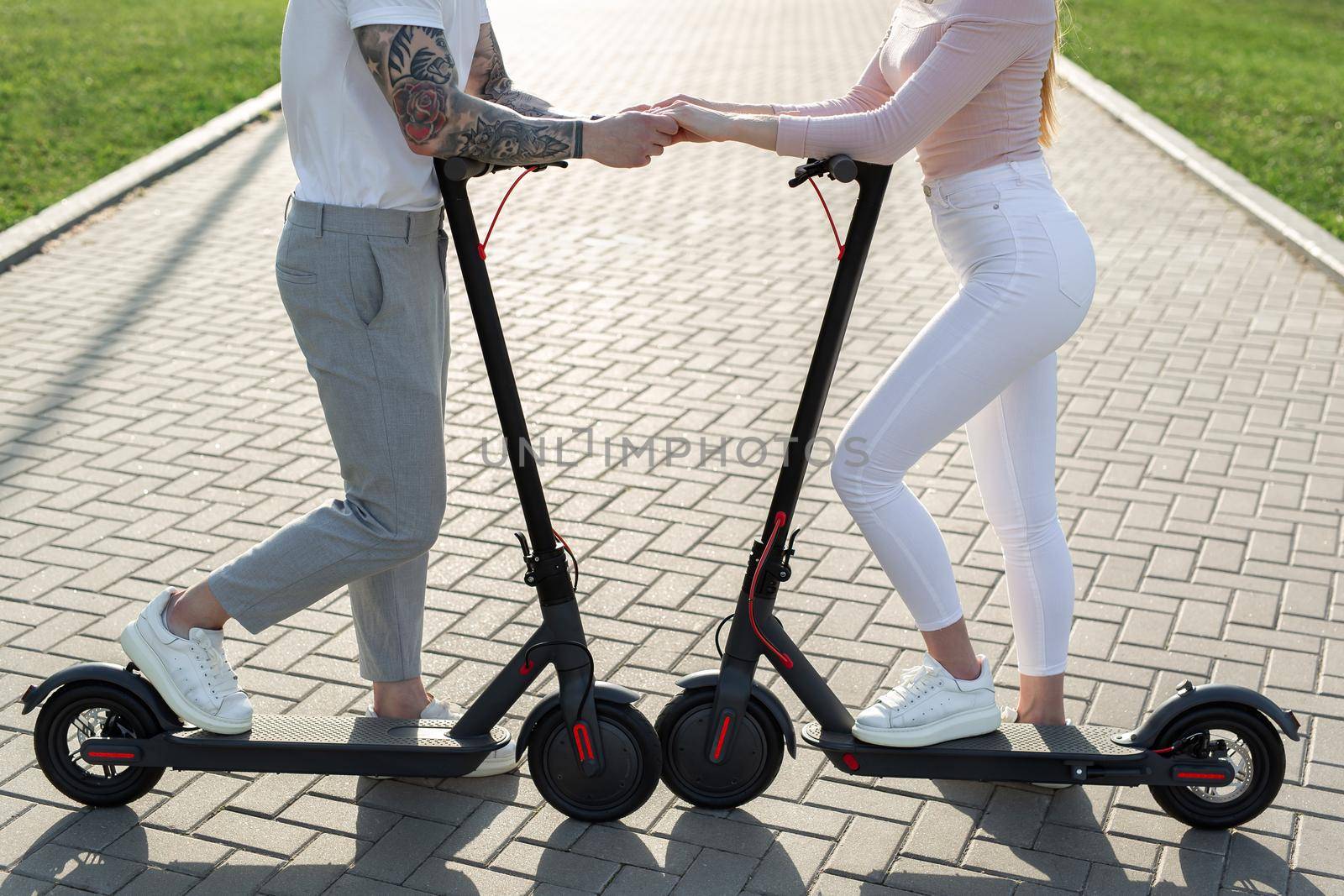 Young couple in the park on electric scooters. by StudioPeace