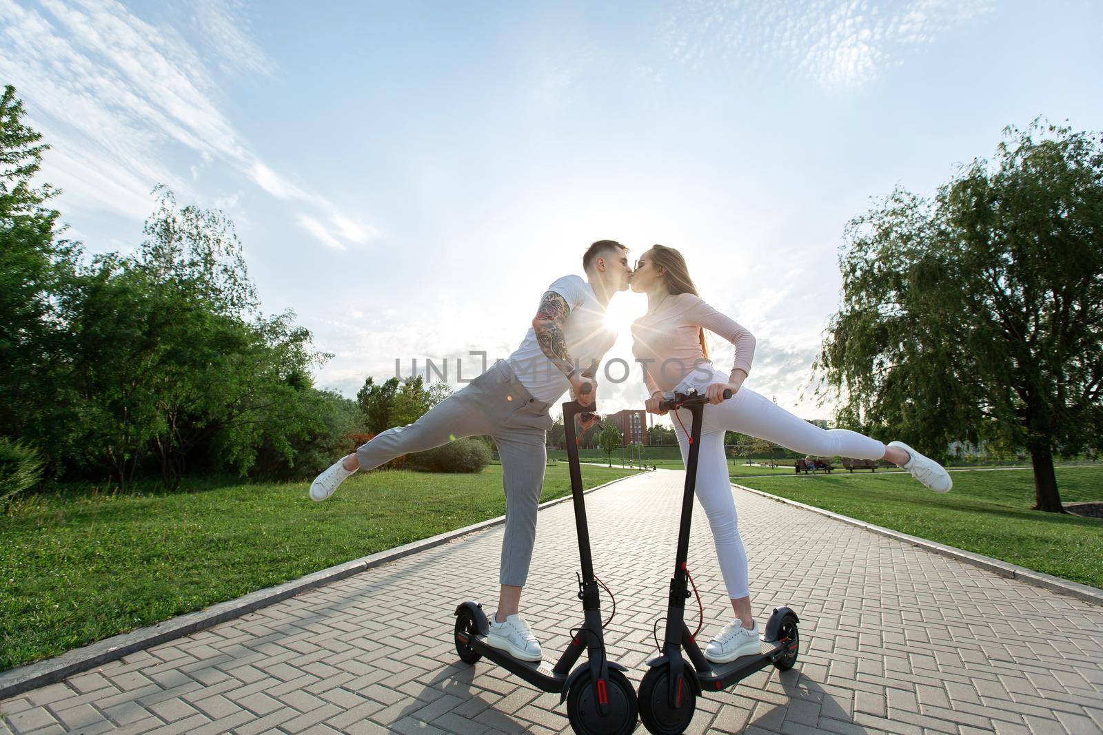 Young couple on vacation having fun driving electric scooter through the park. by StudioPeace