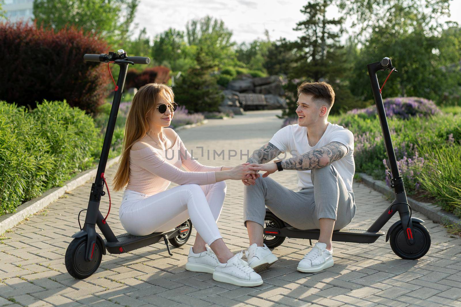 Man and a woman sit on electric scooters in the park