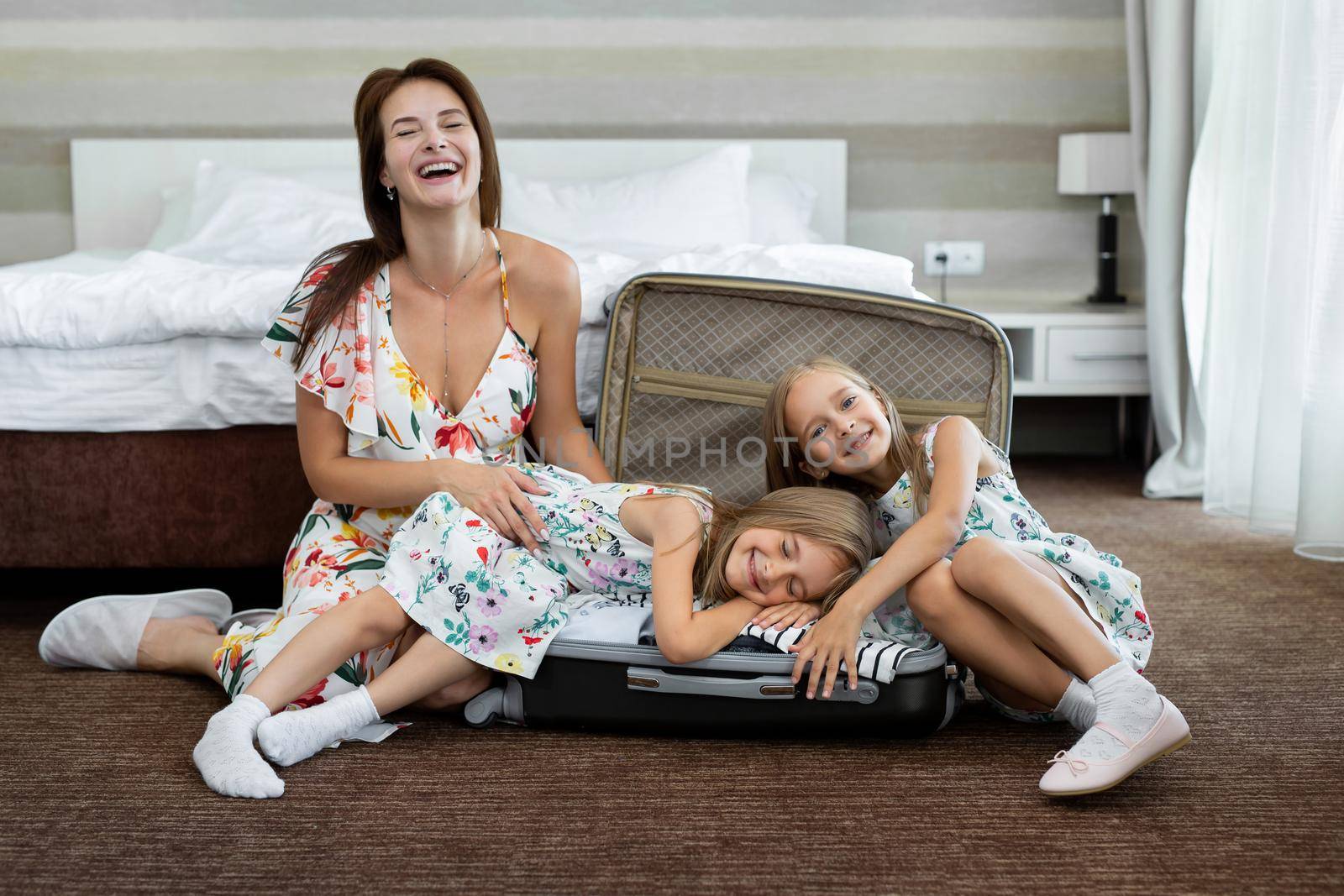 Young mother and her twin daughters with a suitcase in a hotel room by StudioPeace