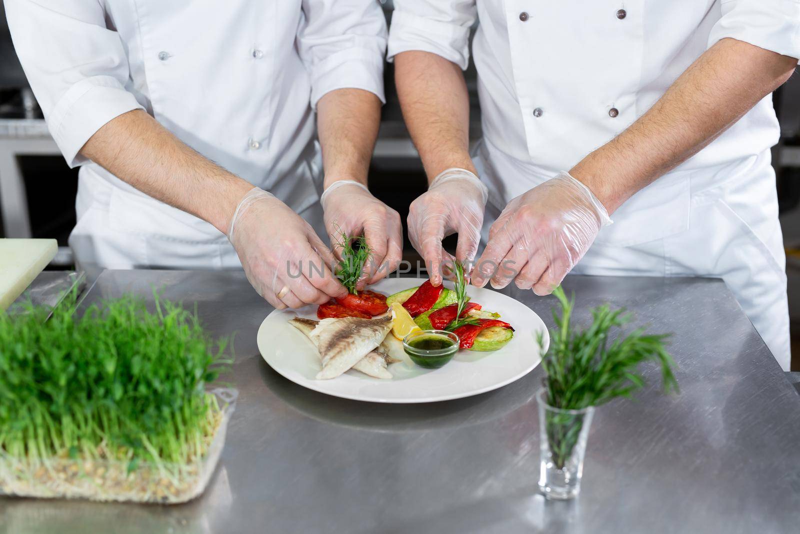 Chef decorates fish from microgreens with vegetables in the kitchen.