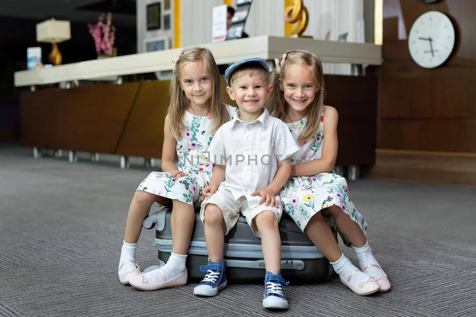 Twin sisters and brother sitting on a suitcase in a hotel.