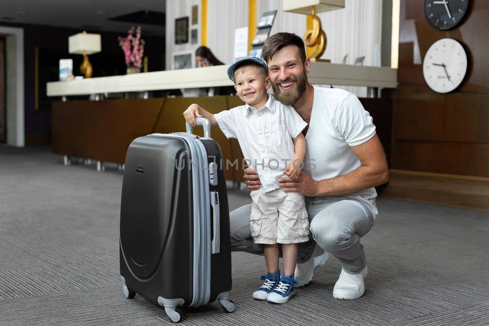 Father and son with a suitcase at the hotel reception by StudioPeace