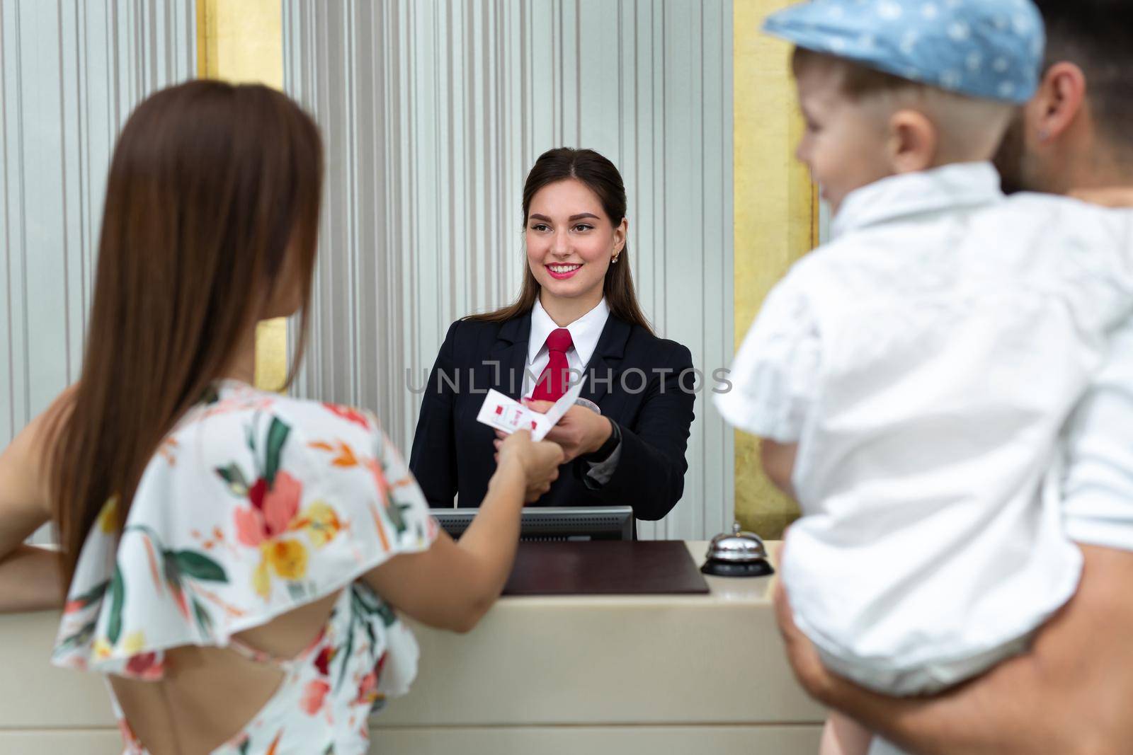 Family with a small son in their arms check in at the hotel and give their passport.