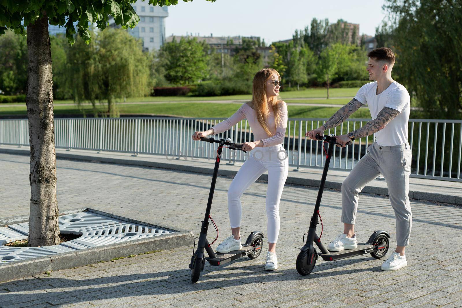 Girl and guy walk on electric scooters around the city, a couple in love on scooters by StudioPeace