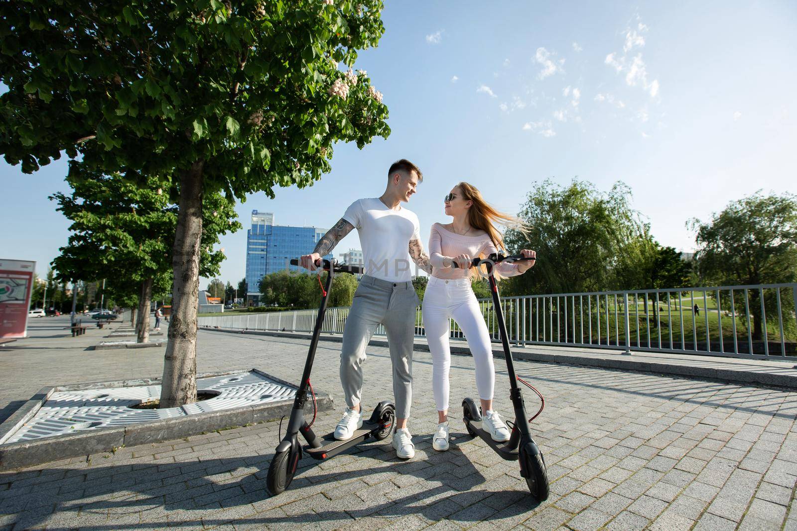 An attractive pair of lovers ride electric scooters and look at each other. by StudioPeace