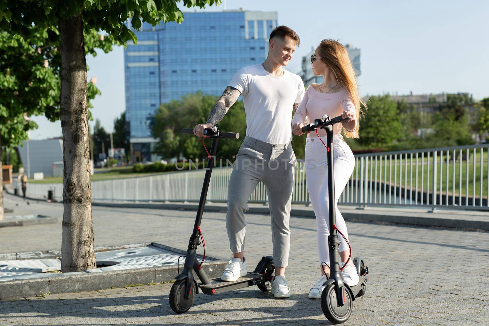 An attractive pair of lovers ride electric scooters and look at each other