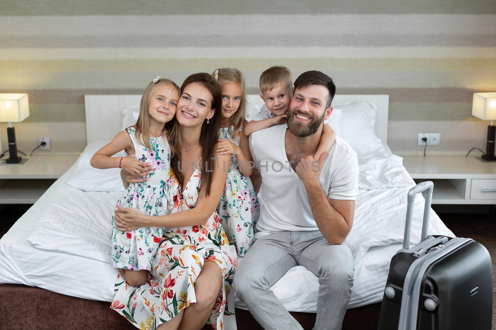 Young family: parents with children sit on the bed in the hotel and laugh. Traveling with children by StudioPeace