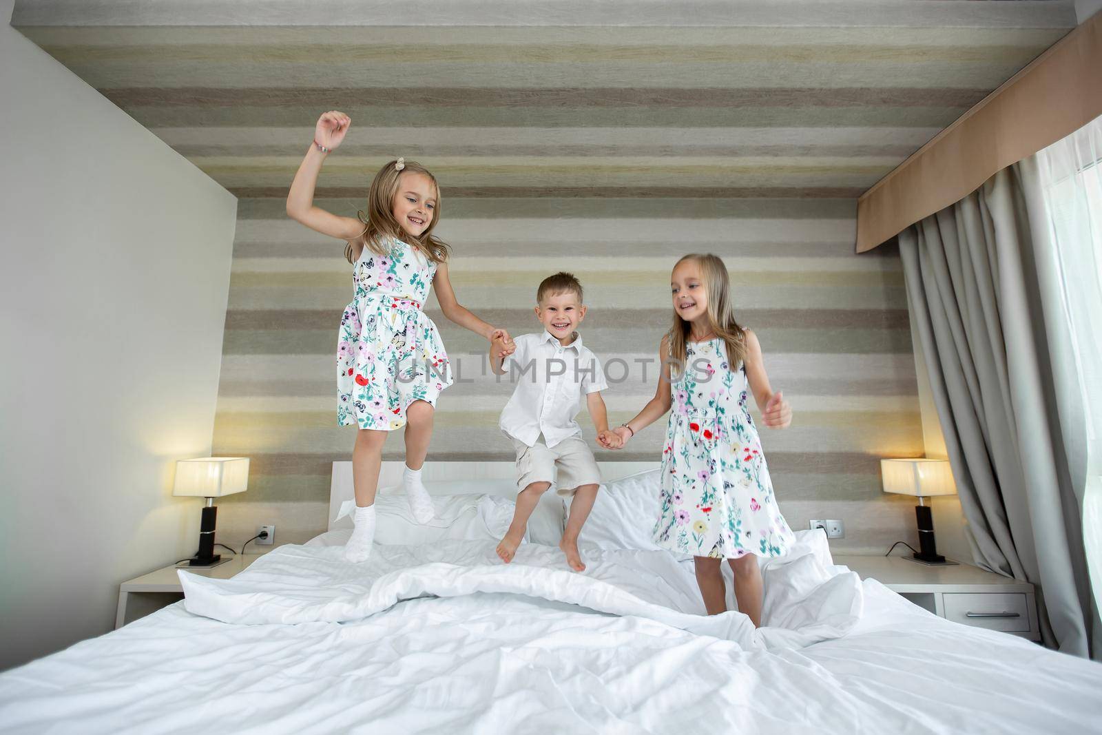 Happy kids jumping, having fun, playing on bed in bedroom