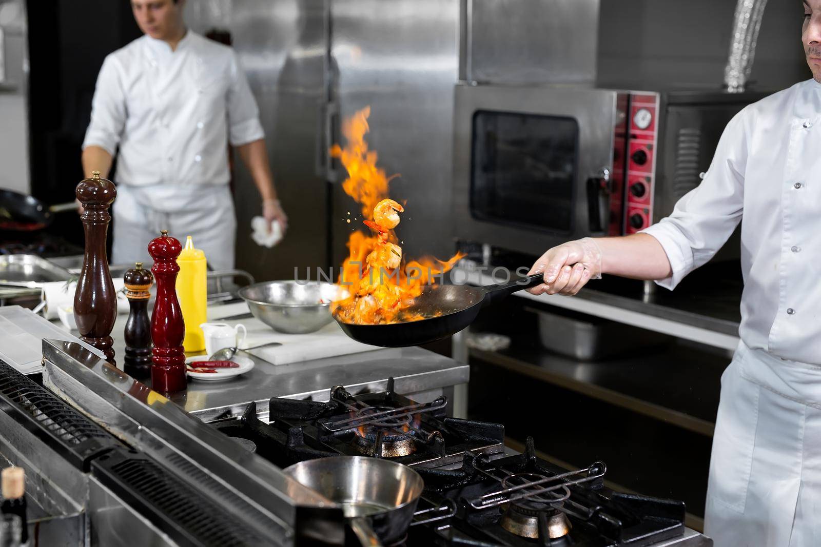 Chef cooking with flame in a frying pan on a kitchen stove. by StudioPeace