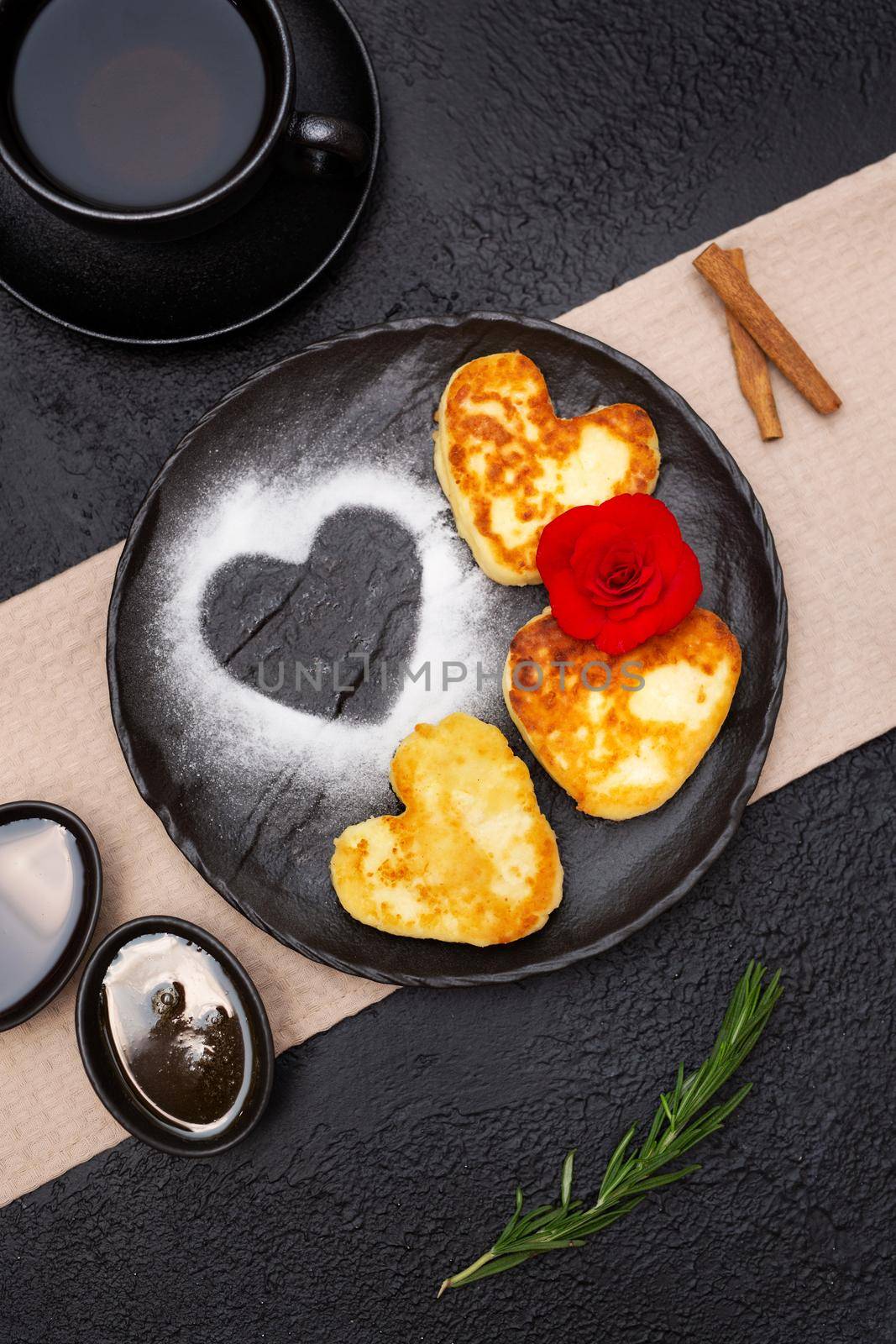 Curd cheesecakes pancakes in the shape of a heart with honey and jam on a black plate