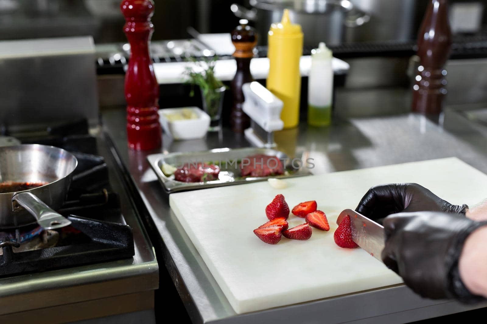 Hand with knife cuts strawberry. Berries on white cooking board. Chef working in the kitchen
