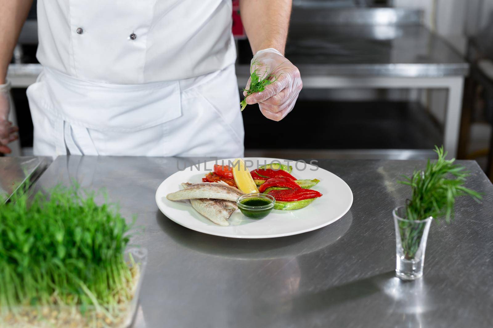 Chef decorates fish from microgreens with vegetables in the kitchen