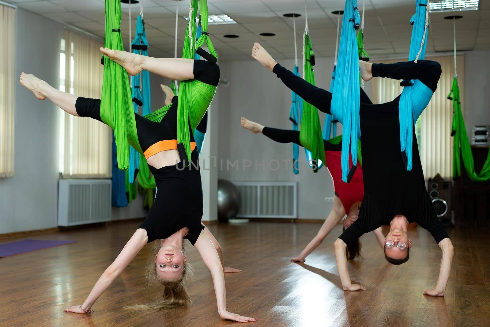 Group of young beautiful yogi women doing aerial yoga practice in hammocks in fitness club by StudioPeace