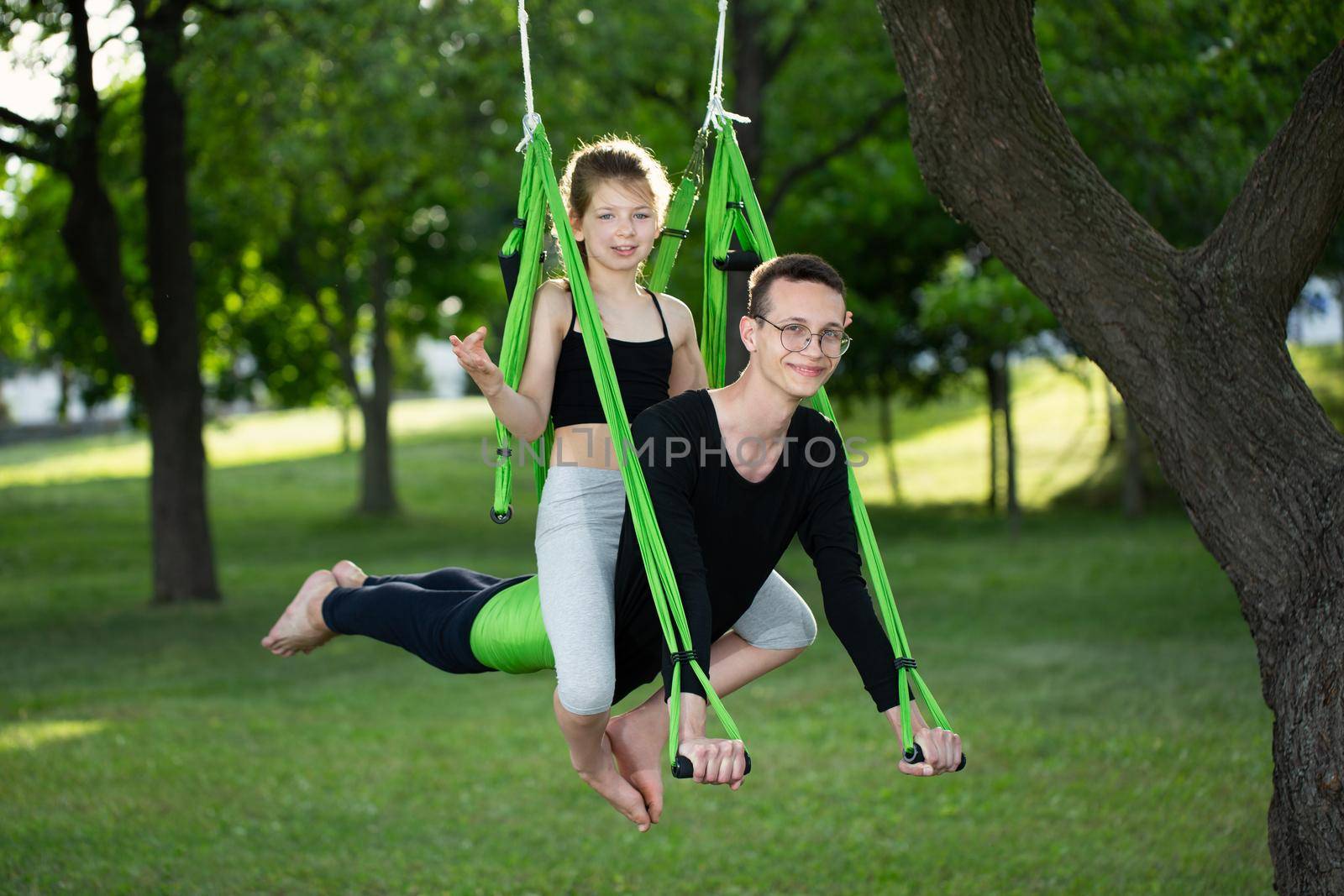 Man and a little girl do group yoga in a hammock in the park