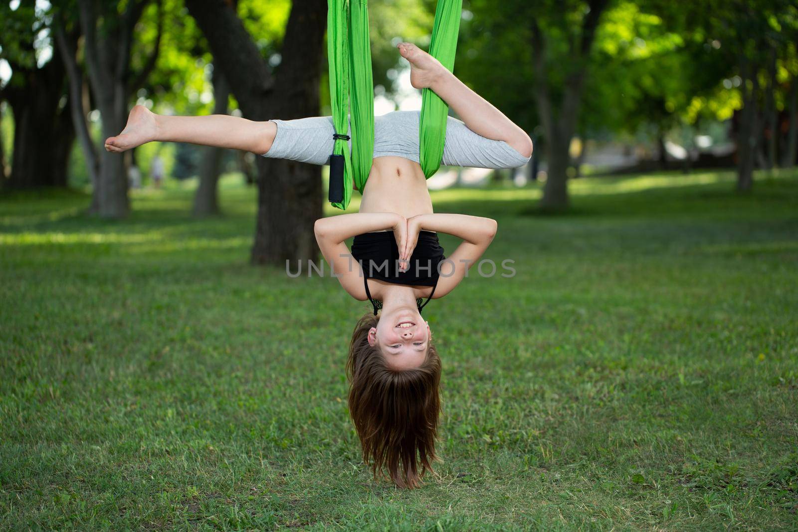 Little girl doing yoga exercises with a hammock in the park. by StudioPeace