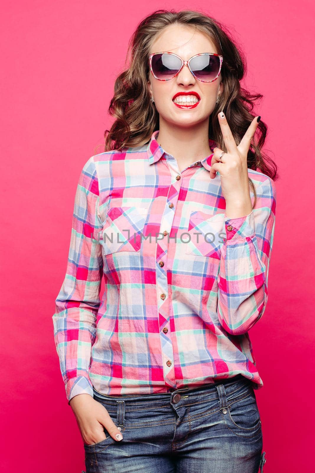 Portrait of emotional girl posing at camera, showing tooth and peace by fingers. Beautiful, swag woman with curly hair,red lips wearing in cheked. Shopping and fashion.