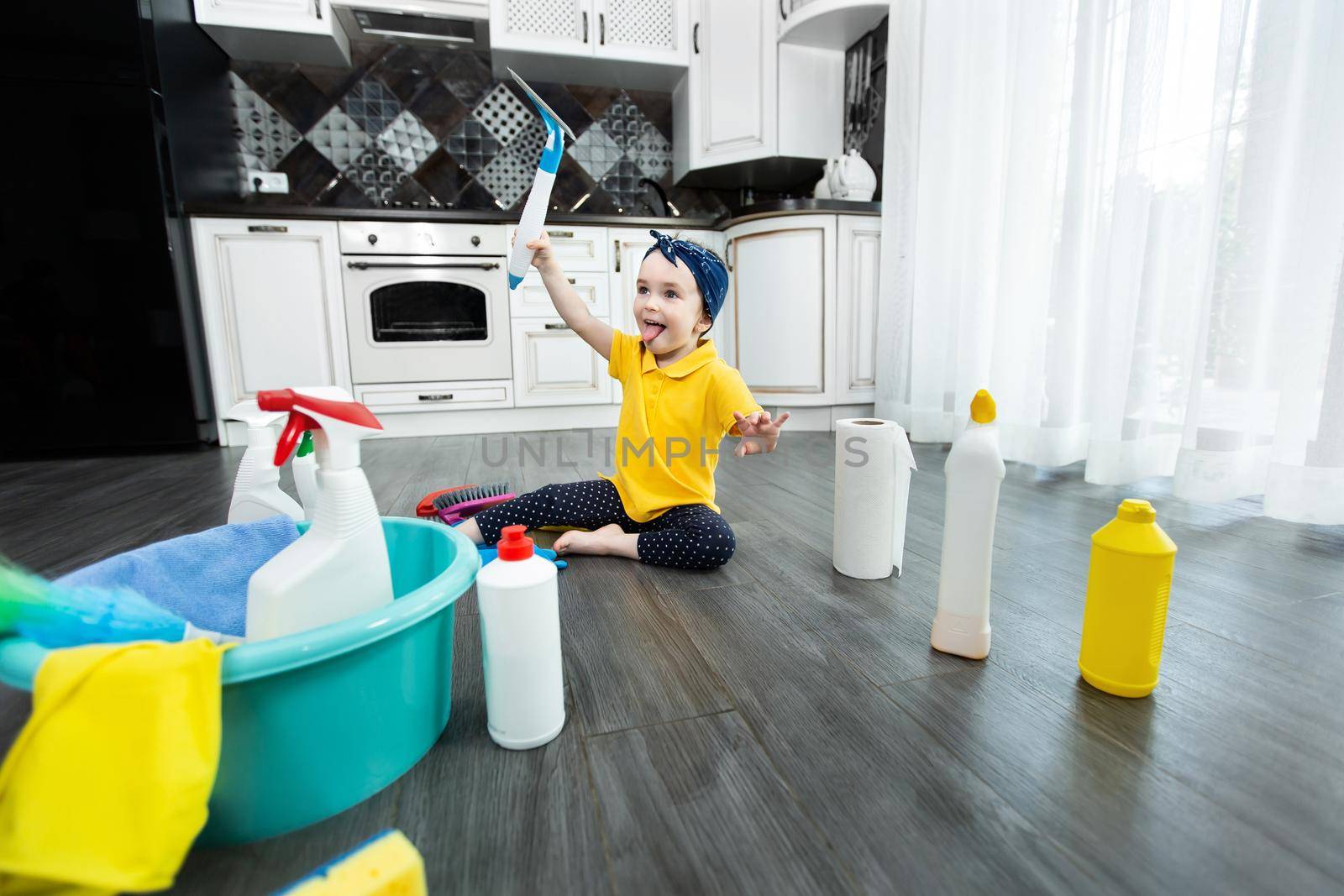 Little girl plays with detergents and a brush on the kitchen floor while cleaning by StudioPeace