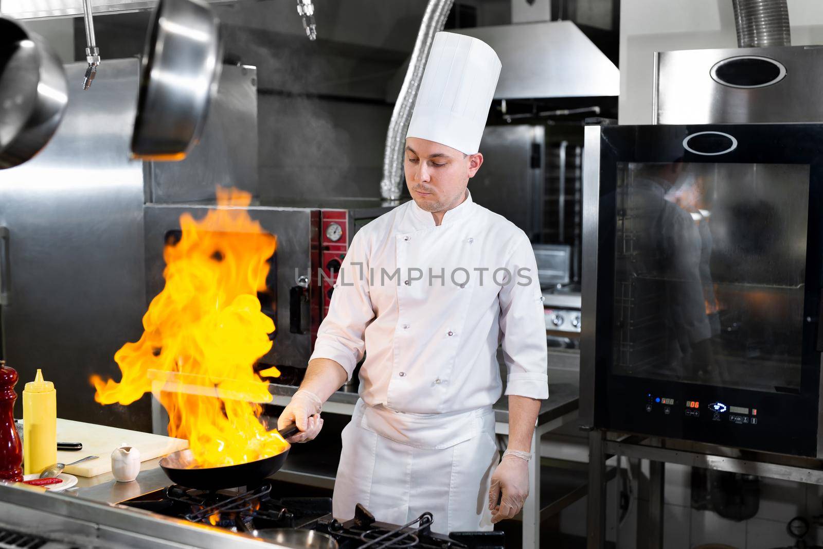 Chef cooking with flame in a frying pan on a kitchen stove