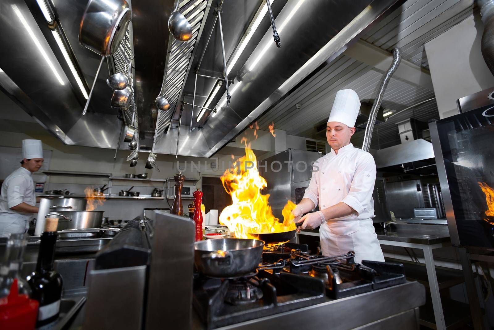 Chef cooking with flame in a frying pan on a kitchen stove. by StudioPeace