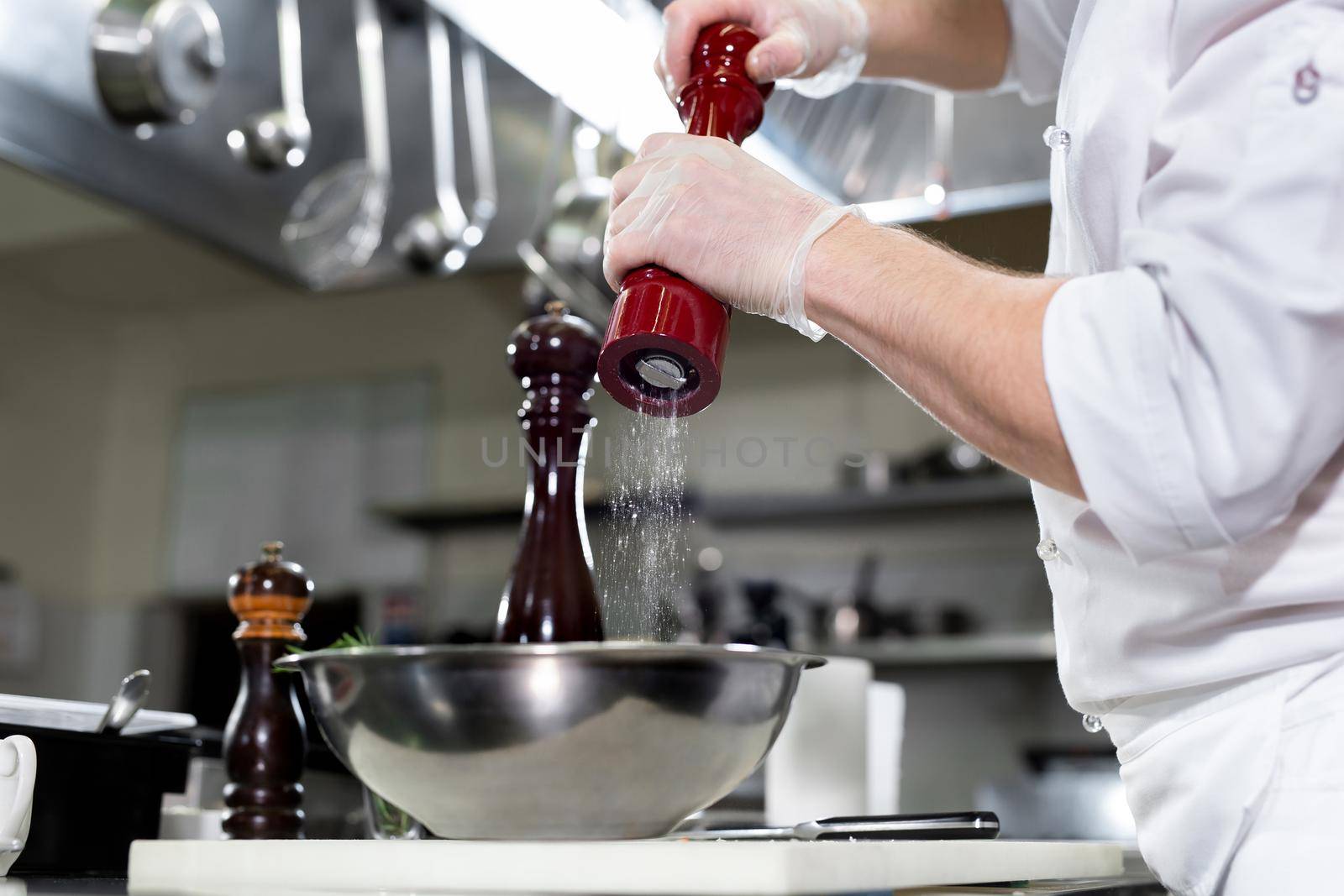 Professional chef in white uniform salts king prawns. Wooden salt grinder. by StudioPeace