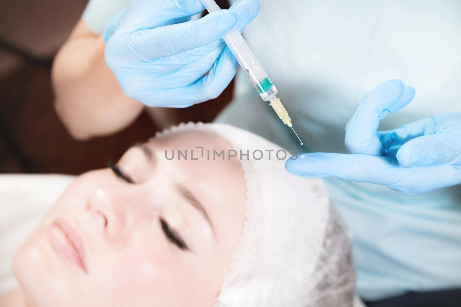 Close-up of a syringe with a drop of botox in the hand of a beautician against the background of the face of a caucasian girl. Injections and injectionology.