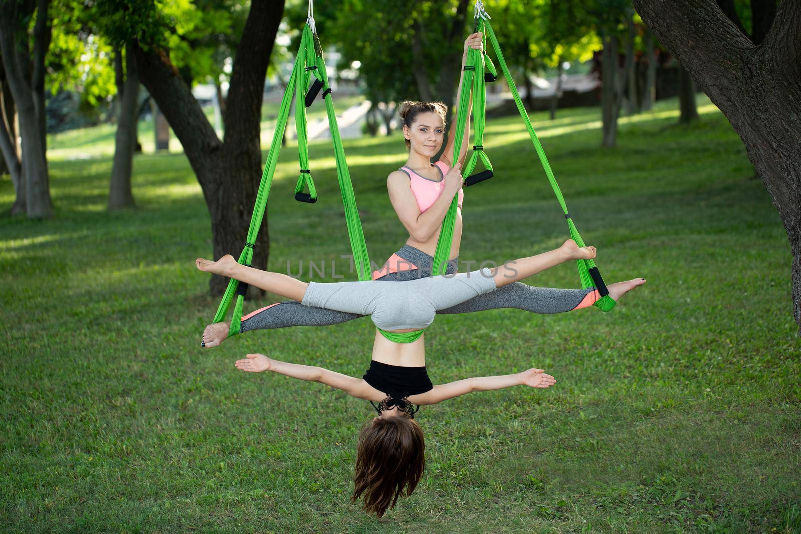 Happy cute young woman doing aerial yoga with her little sister in the park