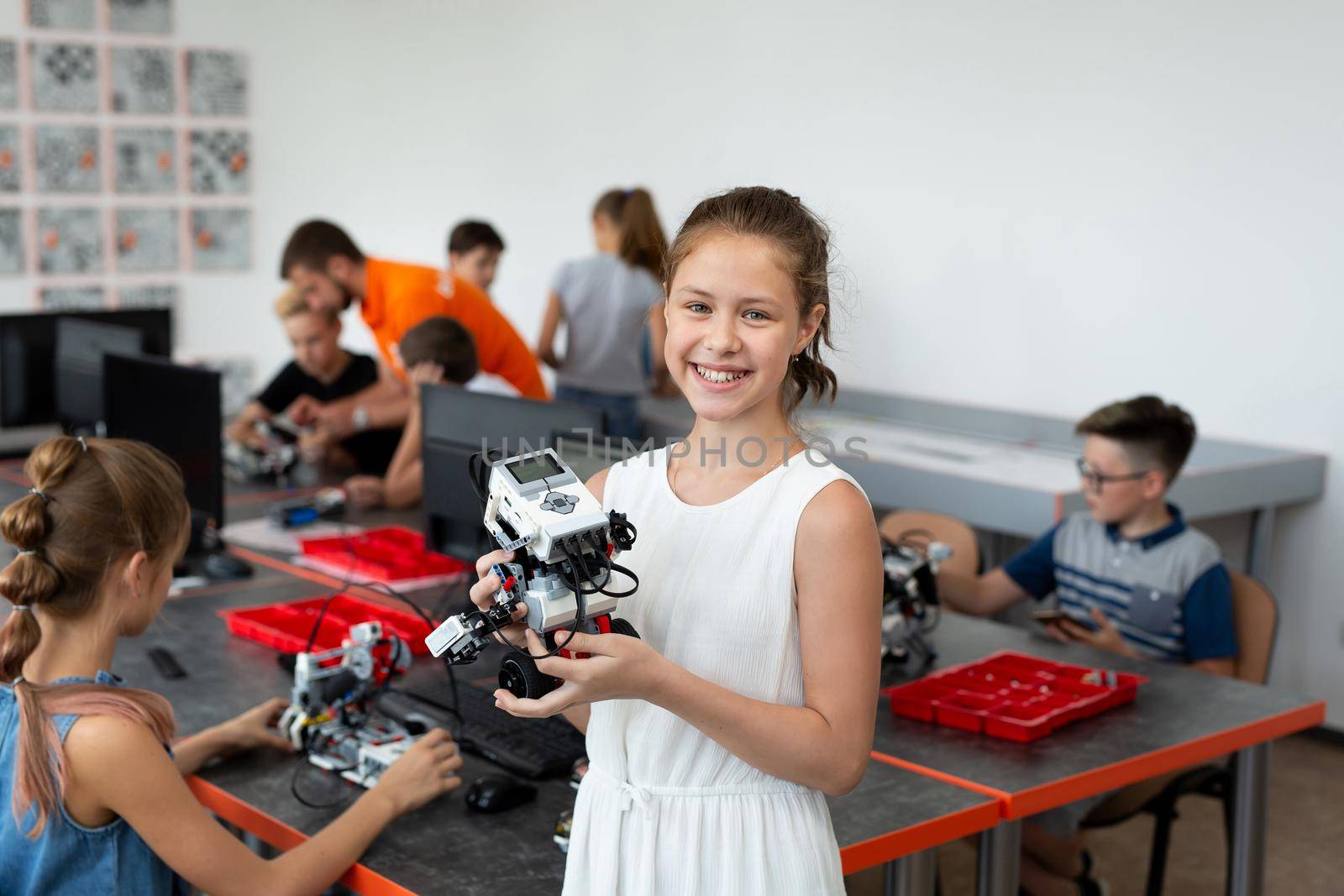 Portrait of a happy schoolgirl girl in a robotics class, she holds a robot assembled from plastic parts programmed on a computer. by StudioPeace