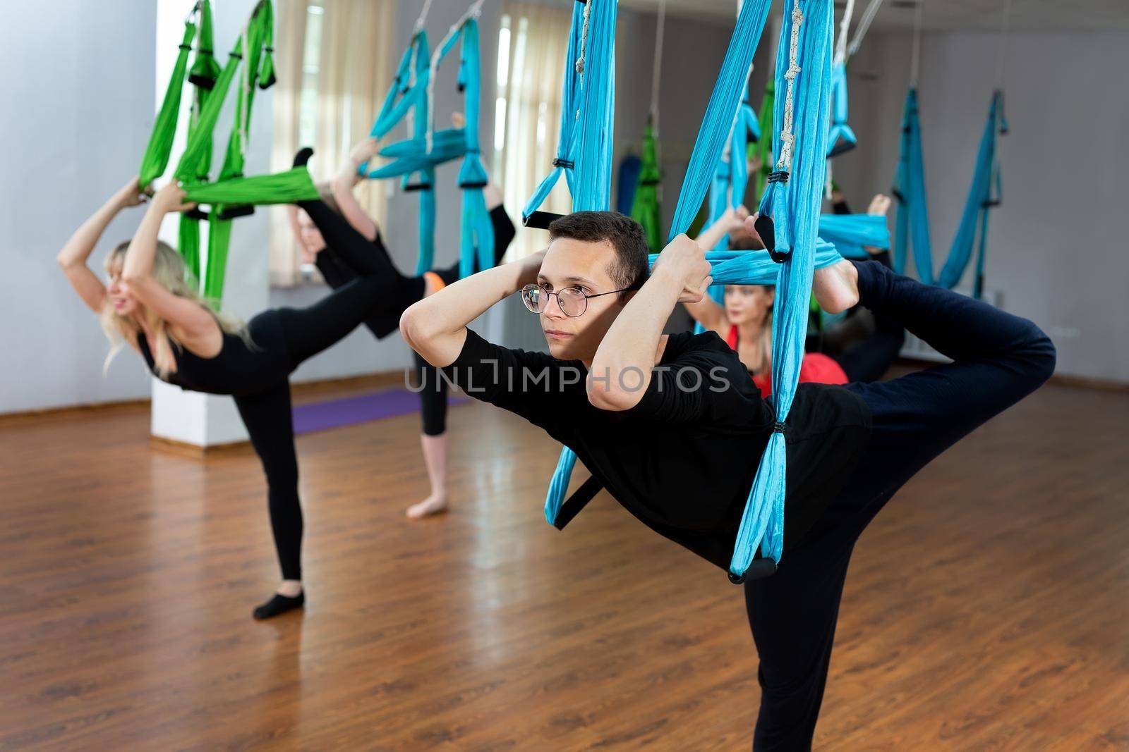 Group of young people practicing yoga on hammock at health club. Fitness, stretch, balance, exercise and healthy lifestyle people by StudioPeace