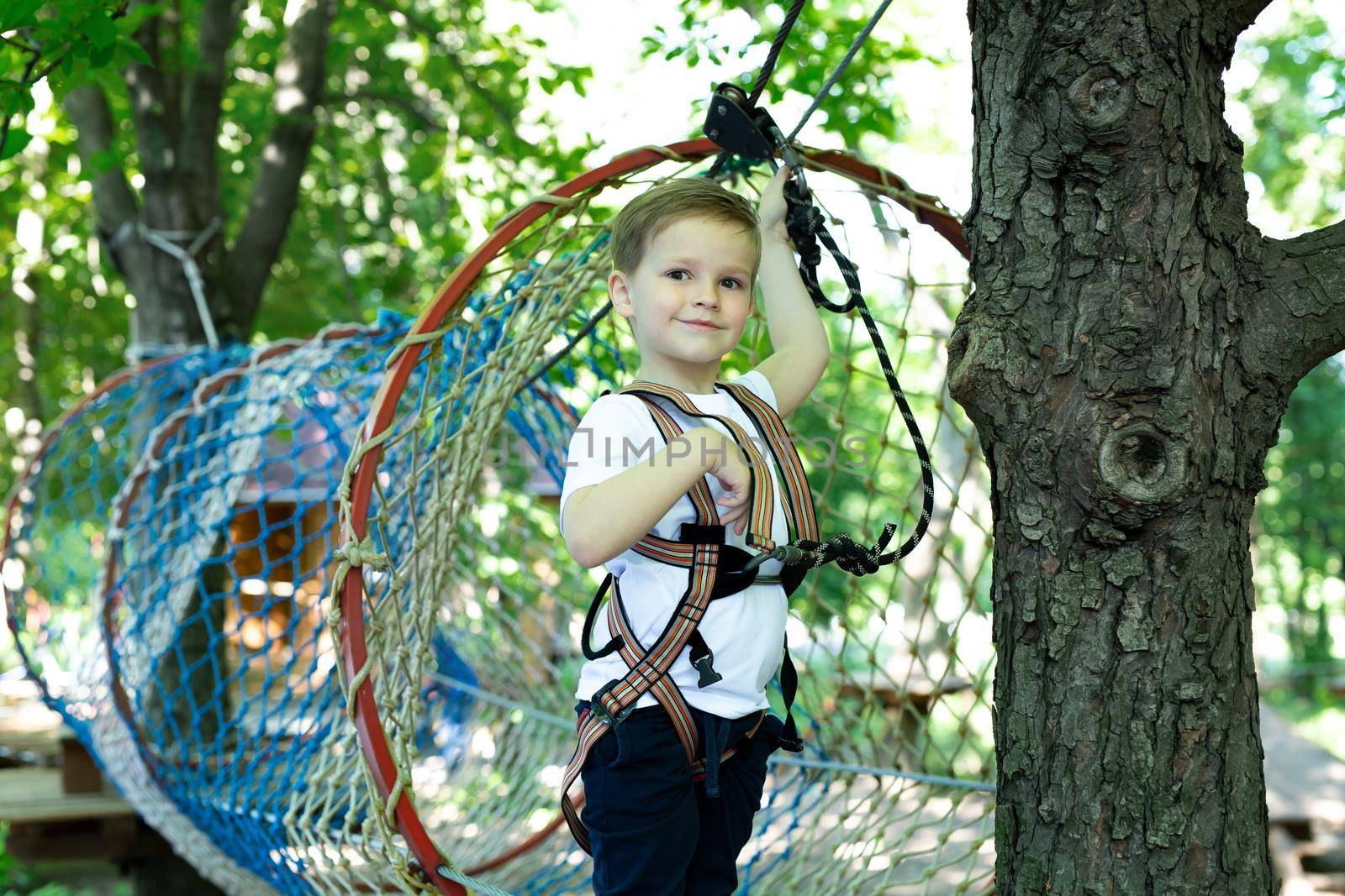 Portrait of a little boy in climbing gear in a rope park, holding a rope with a carbine by StudioPeace