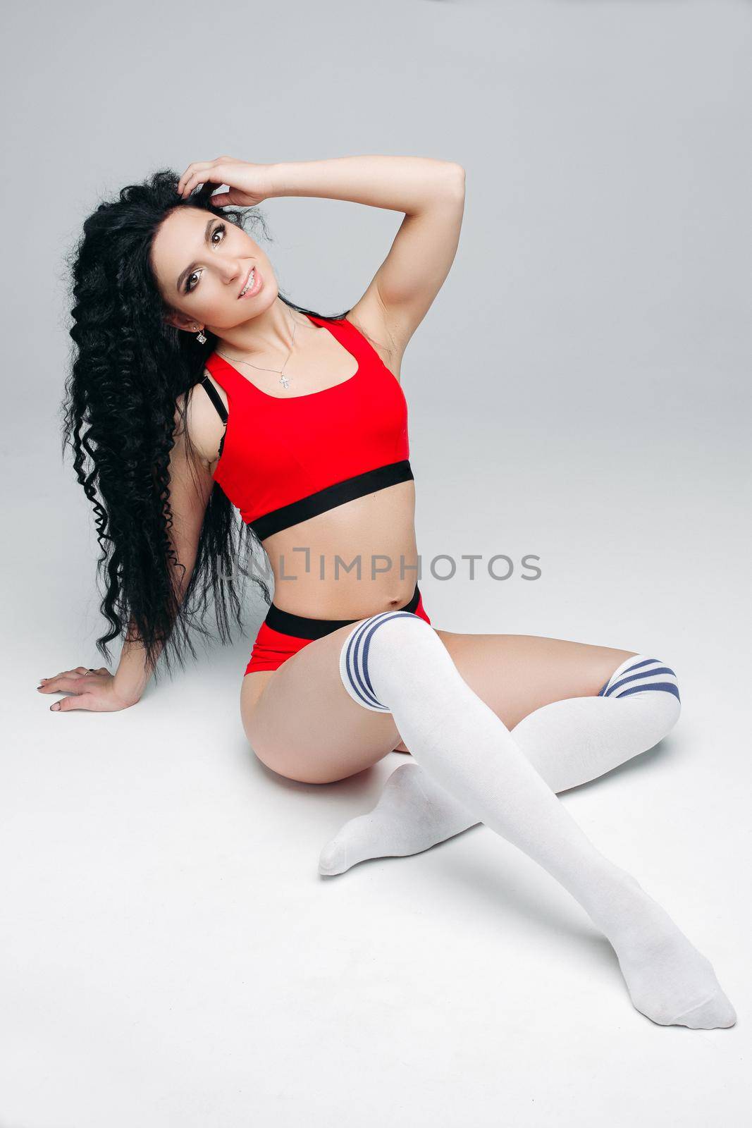 Portrait of sexy attractive and fit brunette, posing at camera with hand up, touching hair. Swag stylish model with curls and red lips at white background. Concept of lifestyle sport and dance.