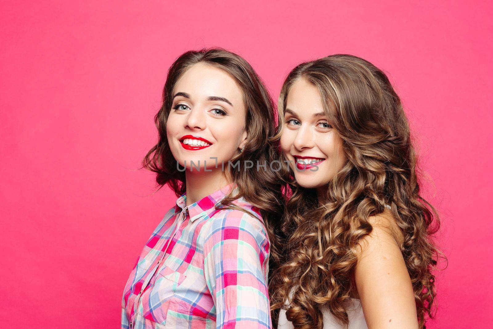 Studio view of beautiful girls with magnificent wavy hair and red lips, in a hipster style with a happy, cute, decomposing smile Isolate on a pink background by StudioLucky