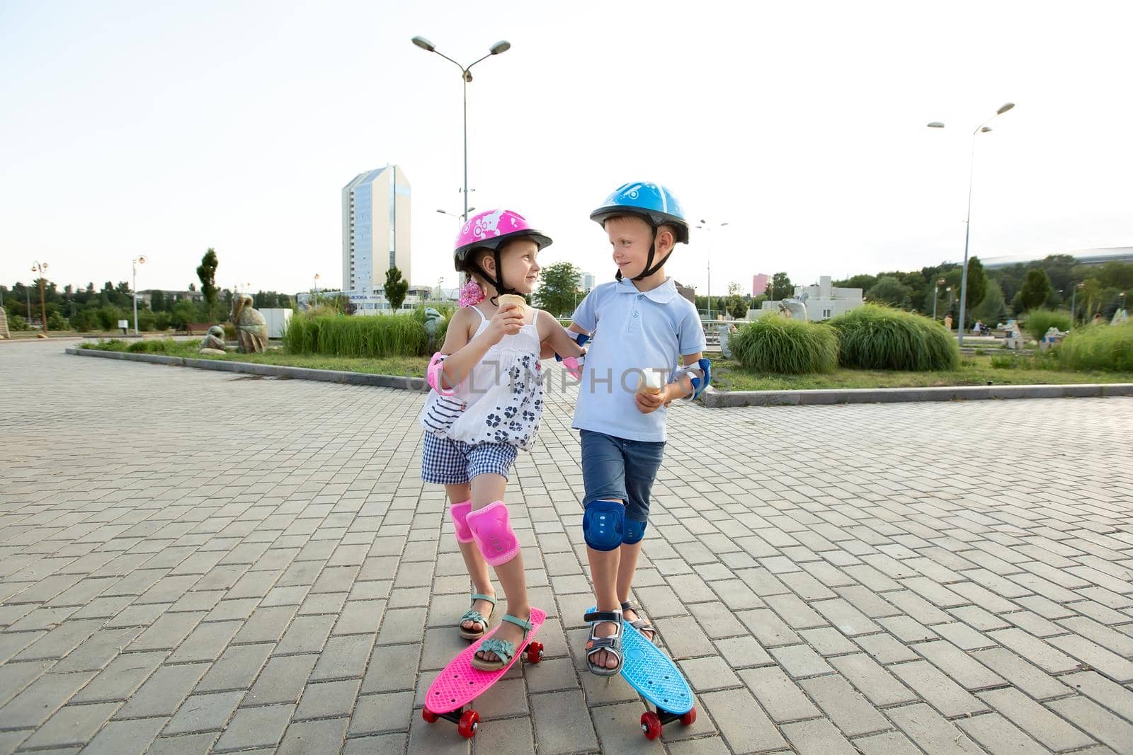 Little boy in a helmet hugs a girl in the Park, they ride a skateboard and eat ice cream