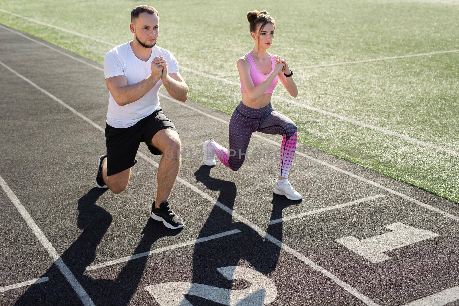 Man and a woman play sports at the stadium in the summer, making lunges. by StudioPeace