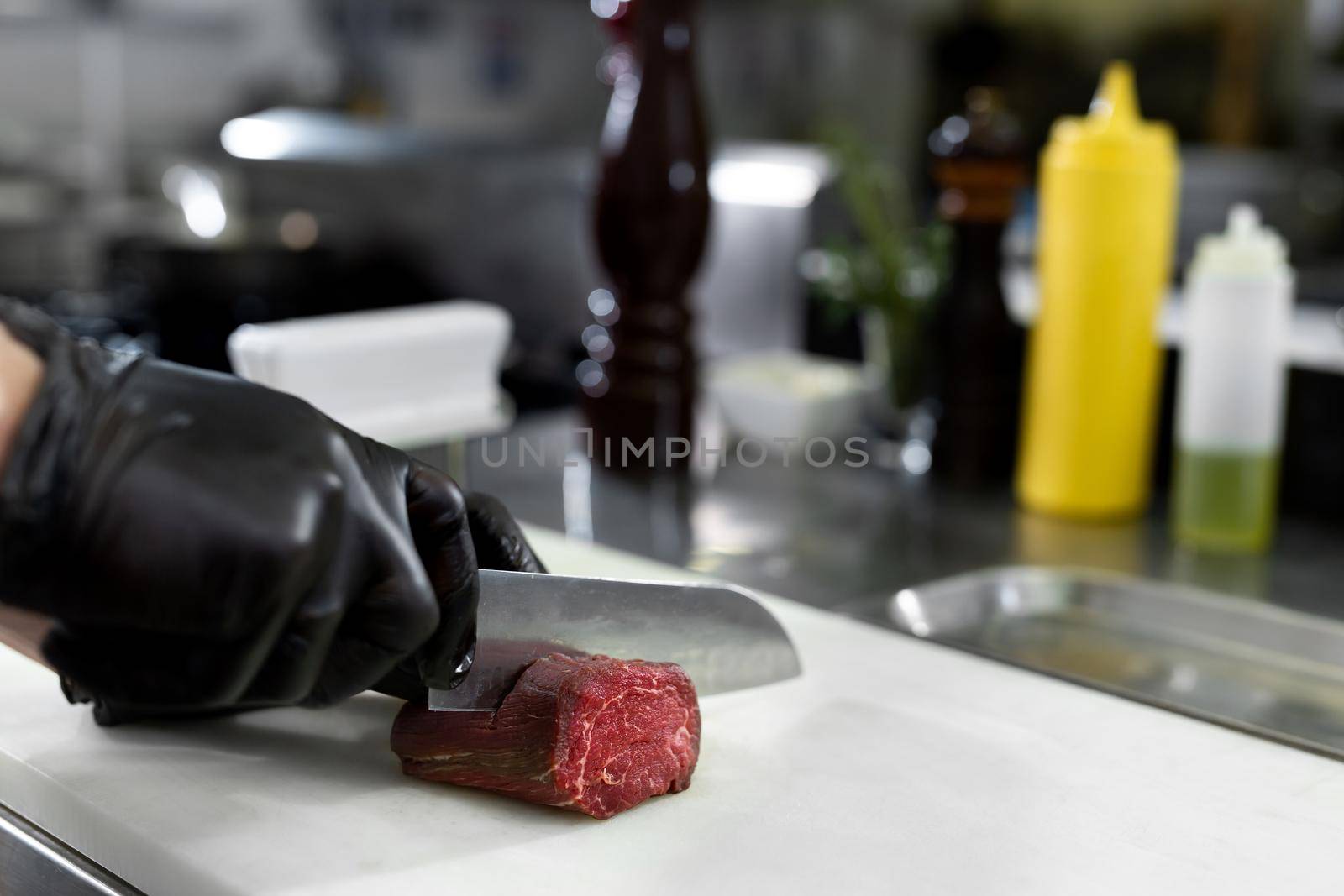 Chef in hotel or restaurant kitchen cooking, only hands, he is cutting meat or steak. by StudioPeace