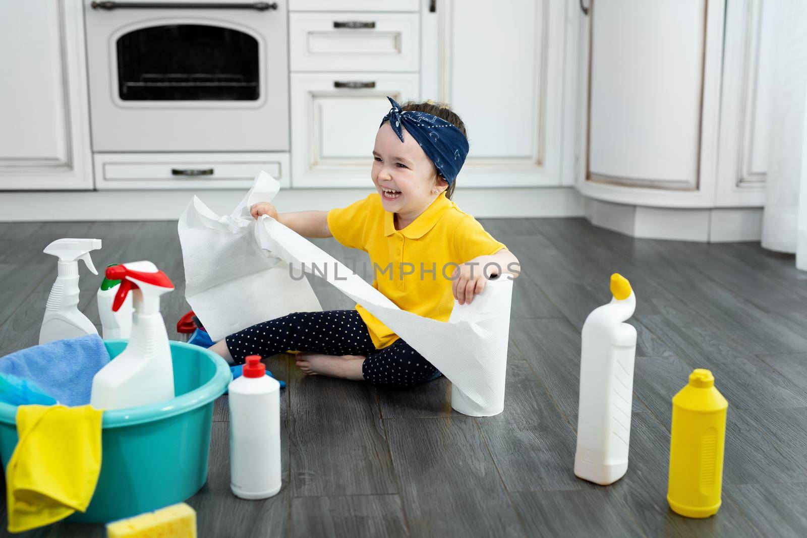 Small girl plays with paper towels in the kitchen while cleaning by StudioPeace