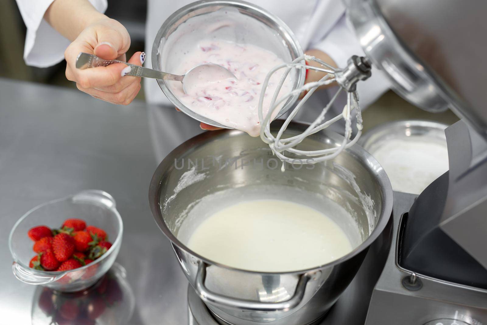 Pastry chef adds cream and strawberries to the bowl of the mixer and knead the dough.