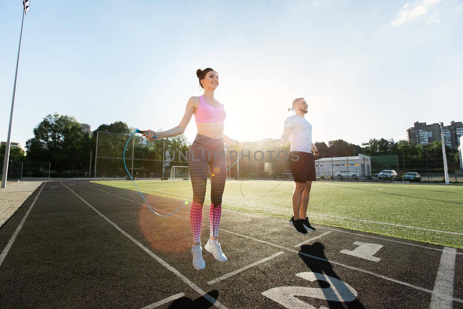 Young fitness couple exercising outdoors at sunset - jumping with skipping rope