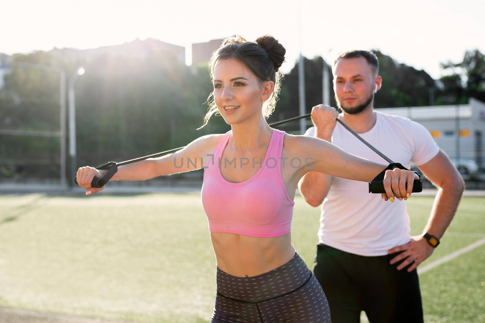 Close-up of young sports people training at the stadium in the summer, a woman doing exercises with an expander and a man helping her