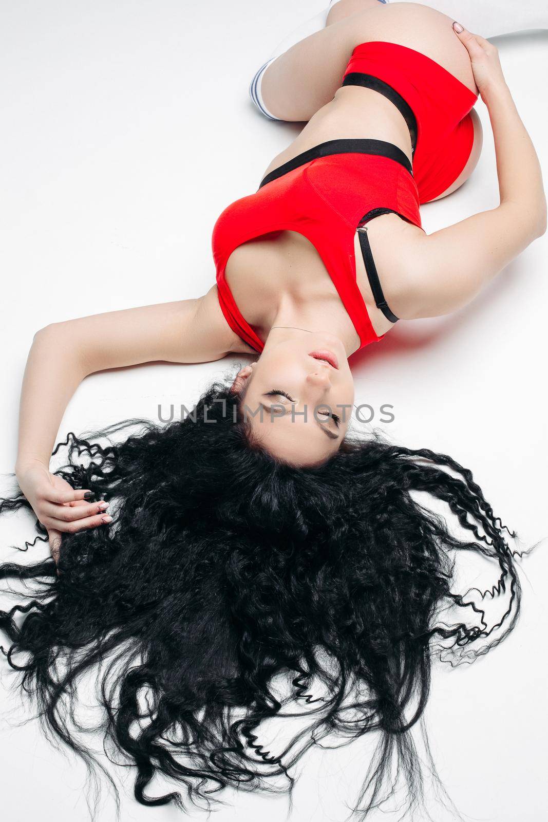 Sexy dark haired girl in red sports wear lying on floor. by StudioLucky