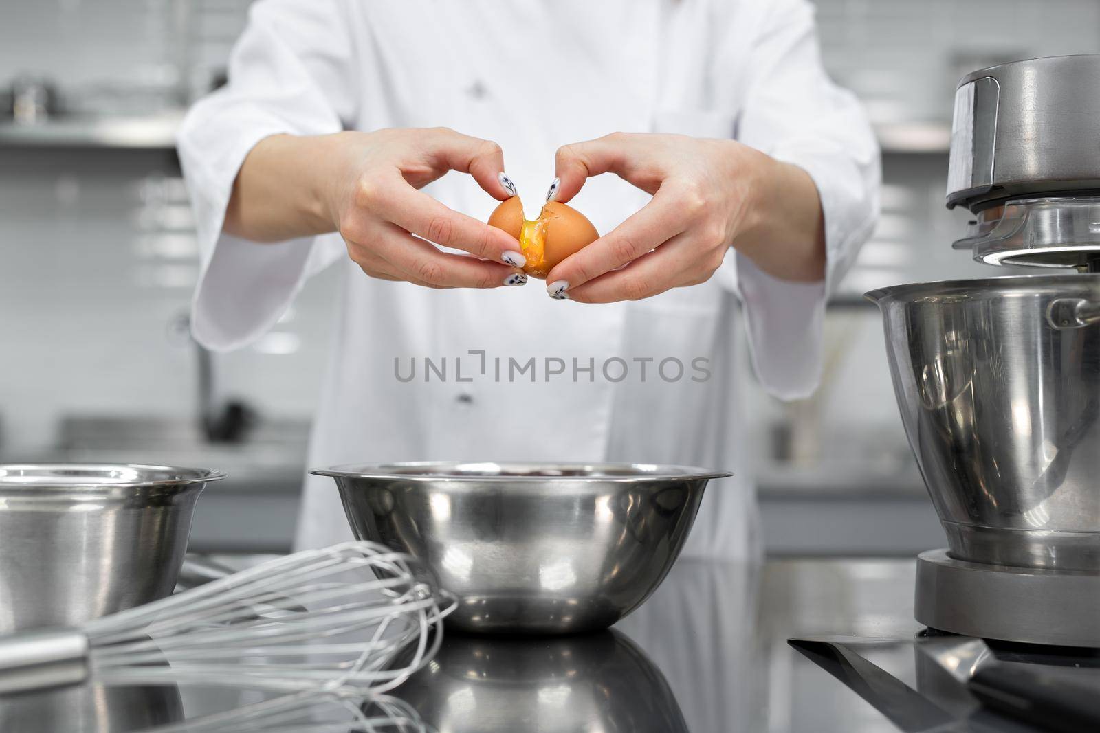 Hands of a pastry chef break an egg in a professional kitchen.