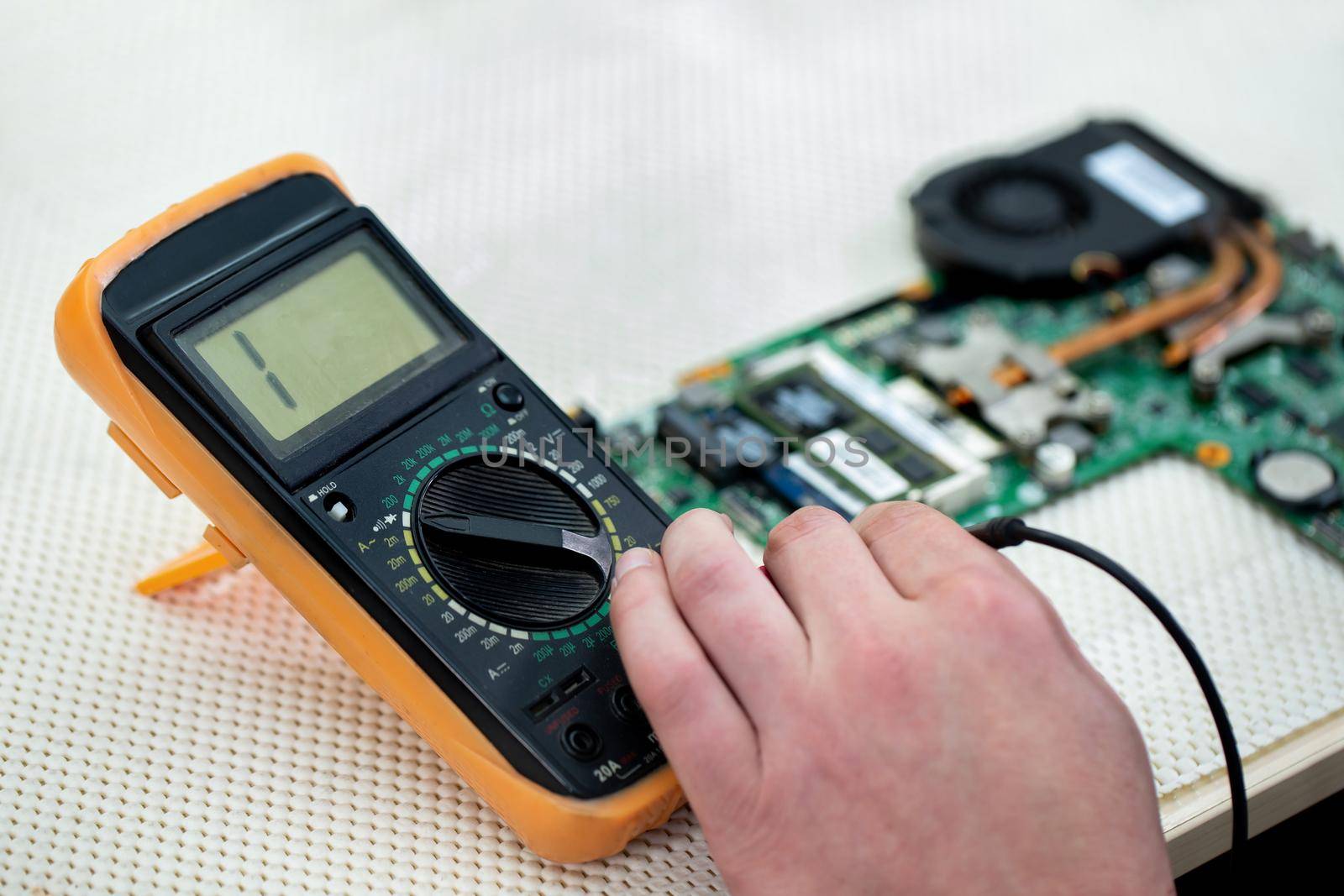 The master checks a broken laptop with a multimeter. by StudioPeace