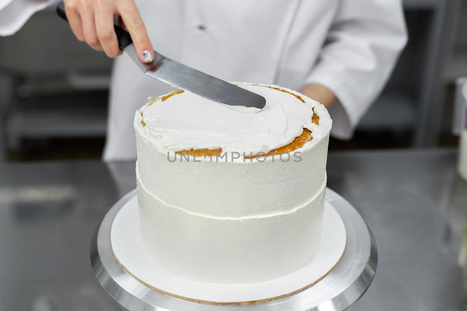 The pastry chef levels the cake with cream. by StudioPeace