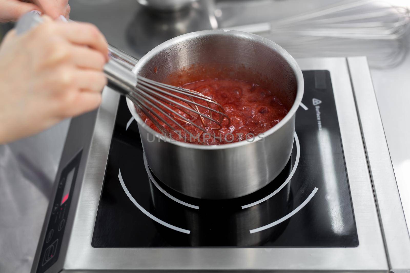 Pastry chef cooks strawberry puree with sugar in a saucepan.