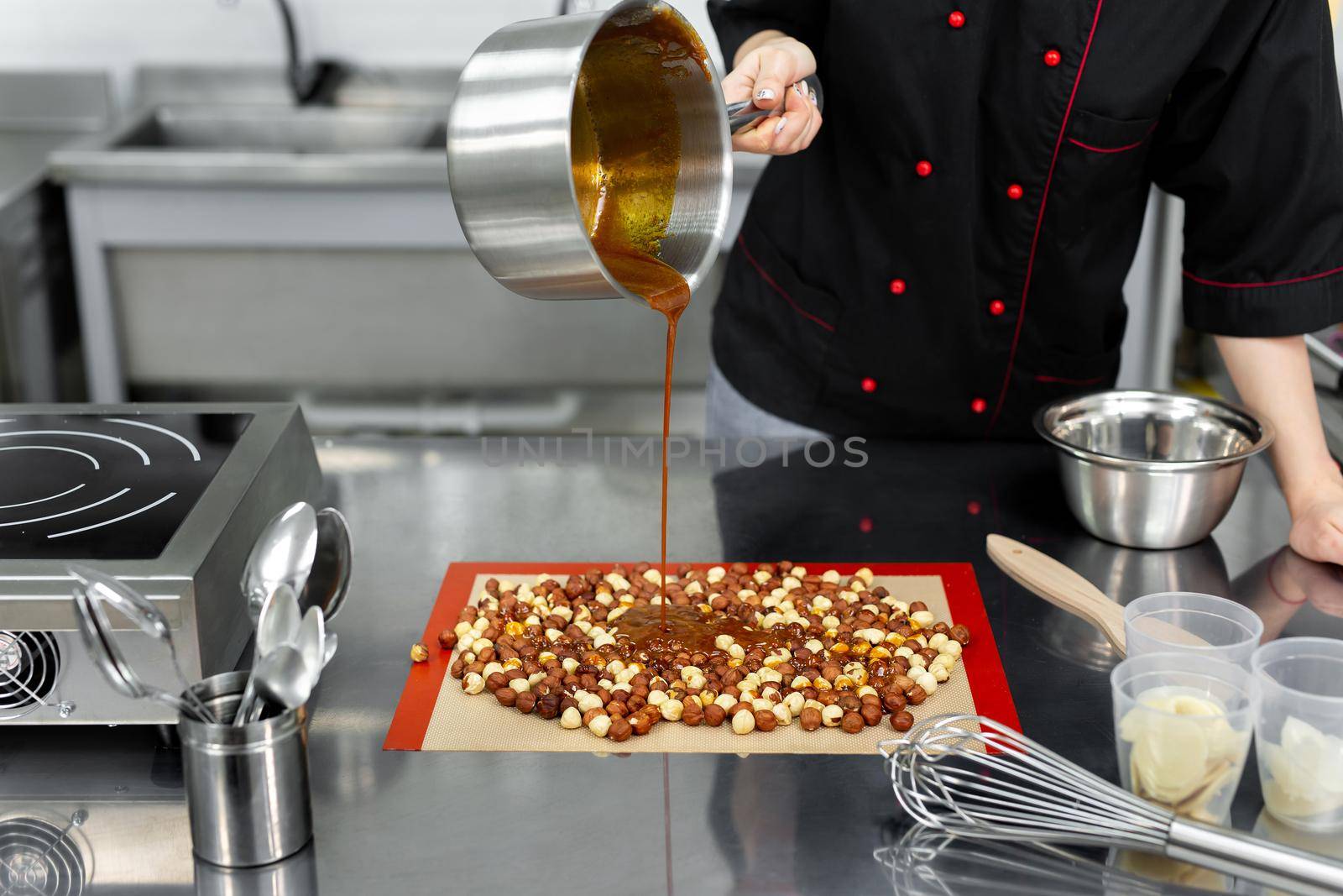 Pastry chef pours hot syrup, caramel on hazelnuts to make praline